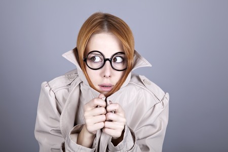 Hiding red-haired girl in glasses and cloak. Studio shot.の写真素材