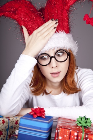 Funny red-haired girl in christmas cap and glasses with gift boxes.の写真素材
