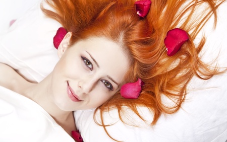 Beautiful red-haired girl in bed with rose petal. Studio shot.の写真素材