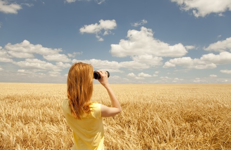 Redhead girl with binocular at wheat field.の写真素材
