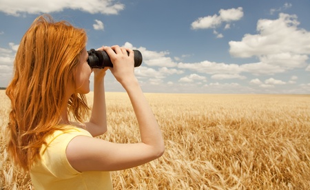 Redhead girl with binocular at wheat field.の写真素材