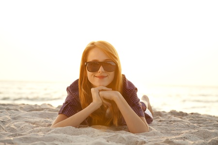 Beautiful redhead girl with headphones at beach sand in sunrise time.の写真素材