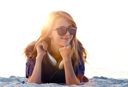 Beautiful redhead girl with headphones at beach sand in sunrise time.の写真素材