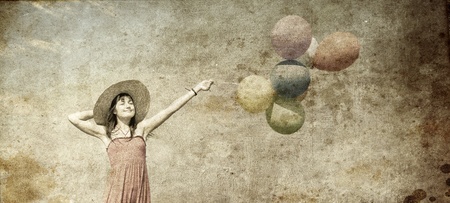 Brunette girl with colour balloons at blue sky background. Photo in old image style.の写真素材