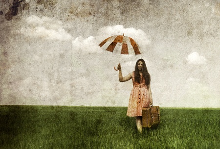 Brunette enchantress with umbrella and suitcase at spring rapeseed field. Photo in old image style.の写真素材