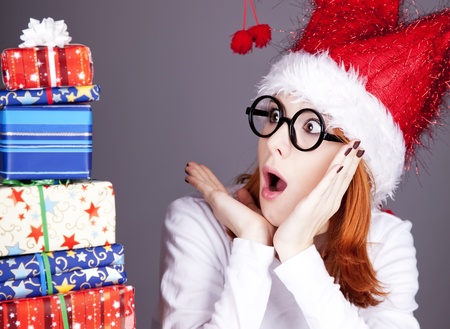 Funny red-haired girl in christmas cap and glasses with gift boxes.の写真素材