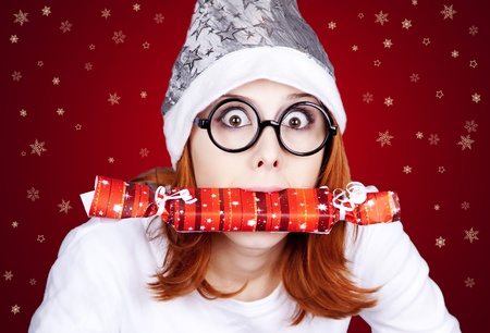 Funny red-haired girl in christmas cap and glasses with gift boxes.の写真素材