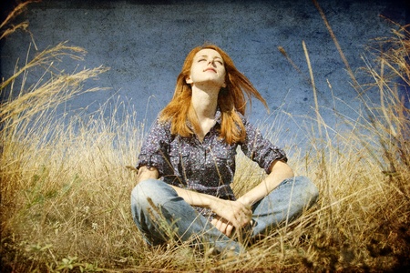 Portrait of happy red-haired girl on autumn grass. Photo in old image style.の写真素材