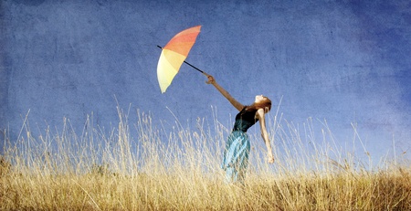Redhead girl with umbrella at windy grass meadow. Photo in old color image style.の写真素材