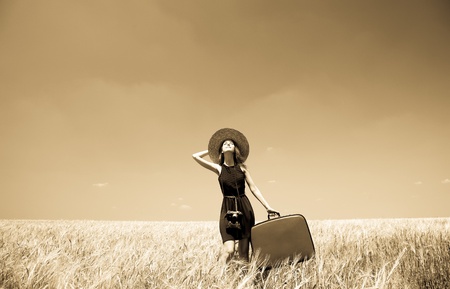 Girl with suitcase at summer wheat field. Photo in old yellow color image style.の写真素材