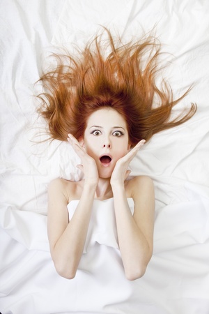 Surprised red-haired girl in bed. Studio shot.の写真素材