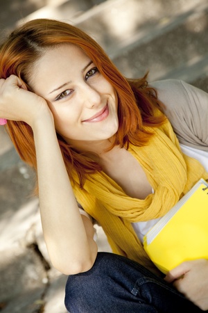 Red-haired student girl with notebook sitting at outdoor.の写真素材