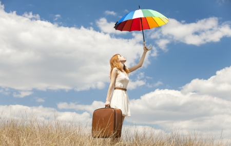 Beautiful redhead girl with umbrella and suitcase at outdoor.の写真素材