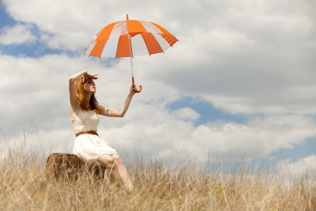 Beautiful redhead girl with umbrella and suitcase at outdoor.の写真素材