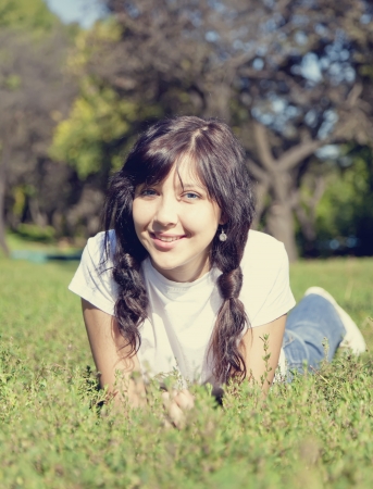 Portrait of beautiful brunette girl with blue eyes on green grass in the park.の写真素材