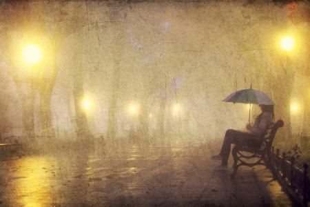 Single girl with umbrella sitting at the bench at nightの写真素材