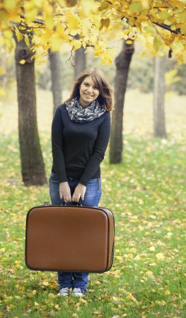 Beautiful girl with suitcase at autumn park. の写真素材