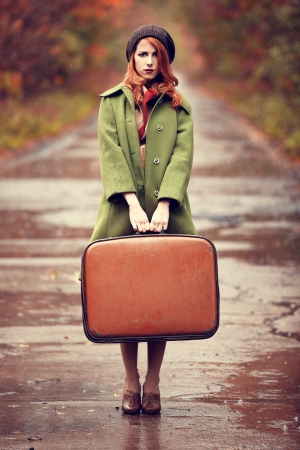 Style redhead girl with suitcase at beautiful autumn alley.の写真素材