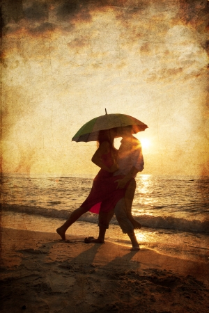 Couple kissing under umbrella at the beach in sunset. Photo in old image style.の写真素材