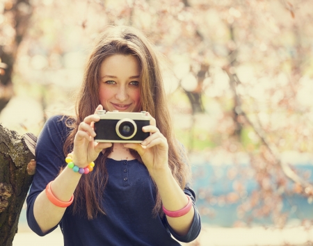 Teen girl in glasses with vintage camera near blossom treeの写真素材