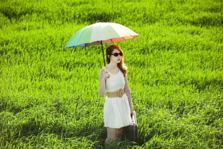 Redhead enchantress with umbrella and suitcase at spring countrysideの写真素材