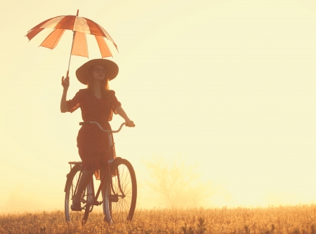 Girl with umbrella on a bike in the countryside in sunrise timeの写真素材