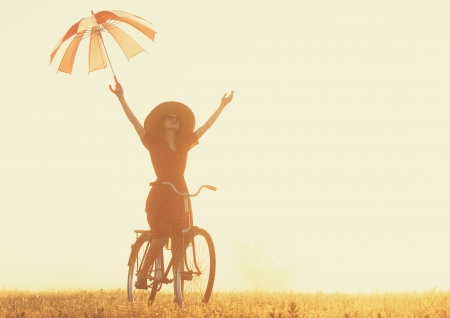 Girl with umbrella on a bike in the countryside in sunrise timeの写真素材
