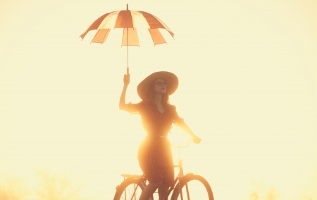 Girl with umbrella on a bike in the countryside in sunrise timeの写真素材