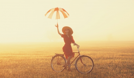 Girl with umbrella on a bike in the countryside in sunrise timeの写真素材