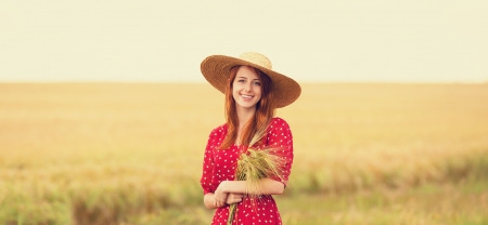Redhead girl in red dress at wheat fieldの写真素材