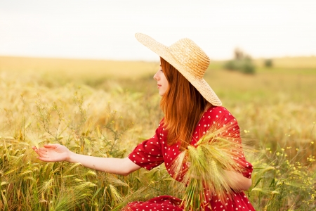 Redhead girl in red dress at wheat fieldの写真素材