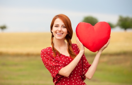 Redhead girl with toy heart at meadow near wheat fieldの写真素材