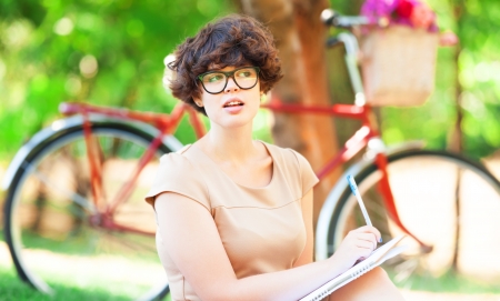 Brunette girl with note in the park. Retro bike at background. の写真素材