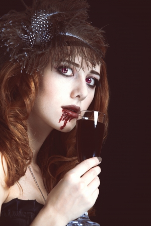 Redhead vampire woman with glass of blood. Photo in vintage style.の写真素材