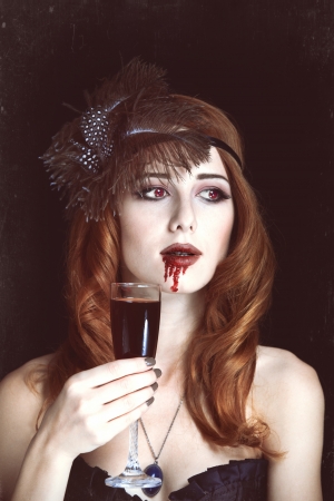 Redhead vampire woman with glass of blood. Photo in vintage style.の写真素材
