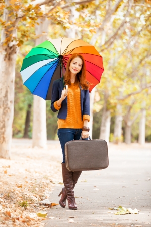 Girl with suitcase and umbrella at autumn outdoorの写真素材