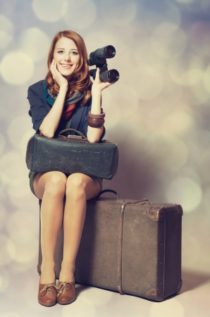 Redhead girl with binocular sitting on the big suitcaseの写真素材