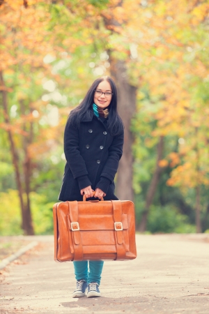 Brunette girl holding suitcase at autumn alley in the parkの写真素材