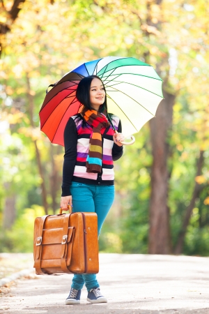 Brunette girl holding suitcase and umbrella at autumn alley in the parkの写真素材
