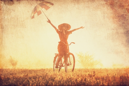 Girl with umbrella on a bike in the countryside in sunrise timeの写真素材