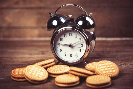 Retro alarm clock with cookie on a table. Photo in retro color image styleの写真素材