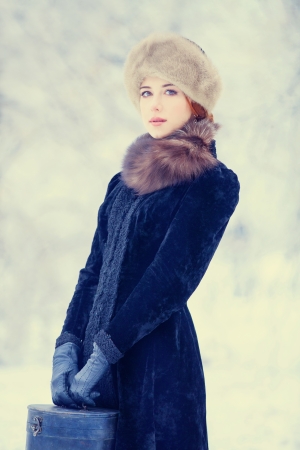 Beautiful redhead women with suitcase in winter park. の写真素材