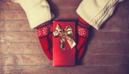 Hands in mittens holding gift box. Photo in old color imagestyle.の写真素材