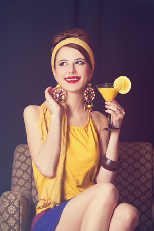 Redhead women sitting in the armchair with cocktail. Photo in retro color style.の写真素材