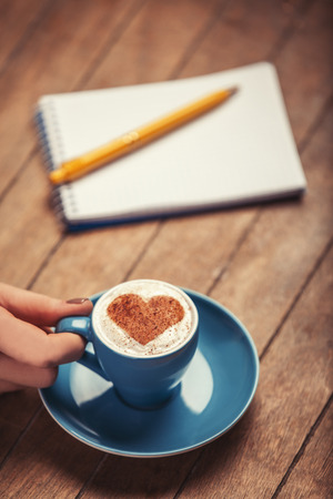 Cup of Ñoffee with shape heart and note with pen on a wooden table.の写真素材