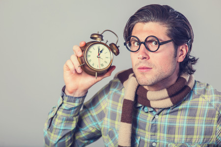 Portrait of funny man in glasses with alarm clock on gray background.の写真素材