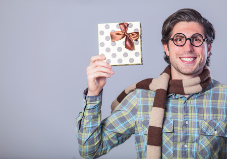 Portrait of funny man in glasses with gift on a gray background.の写真素材