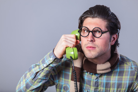 Portrait of funny man in glasses with telephone on a gray background.の写真素材