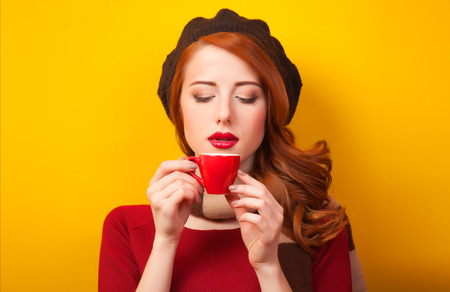 Redhead girl with red cup of coffee or tea on yellow background.の写真素材