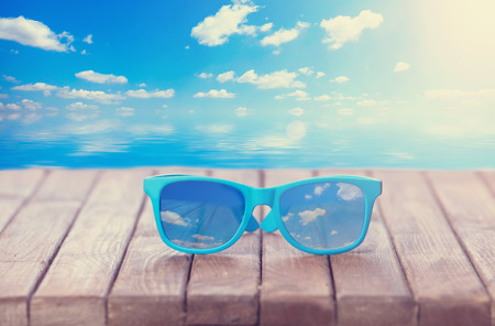 Sunglasses on wooden table and the sea on background.
